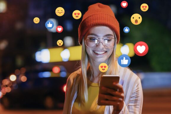 Młoda kobieta, obserwująca media społecznościowe na smartfonie.